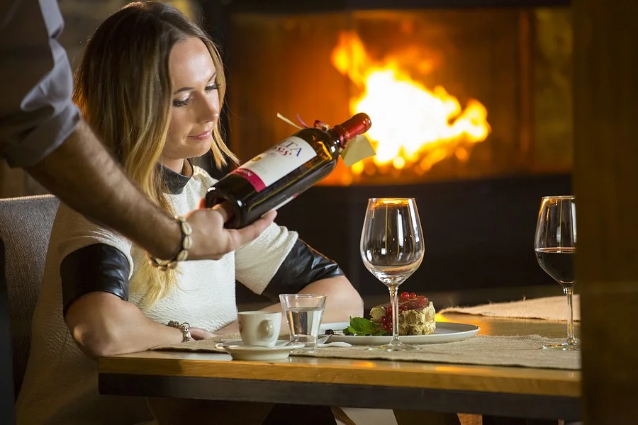 Kelner nalewa czerwone wino gościni przy kominku w Villa Toscana