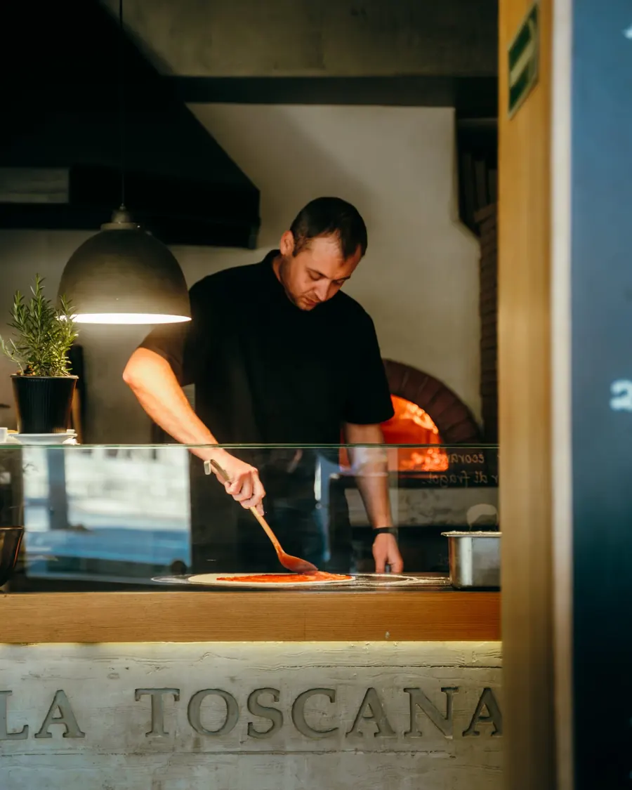 Pizzaiolo wkłada pizzę do pieca opalanego drewnem w Villa Toscana Zakopane